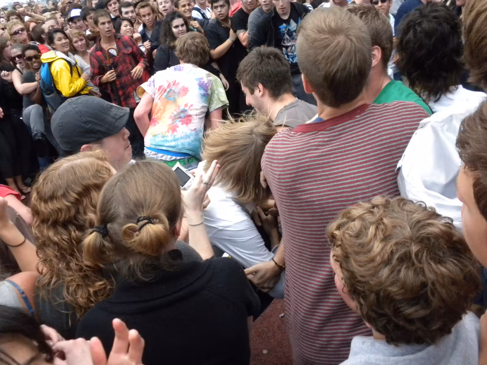 A crowd of fans crammed together with arms raised in a mosh pit at an outdoor festival.