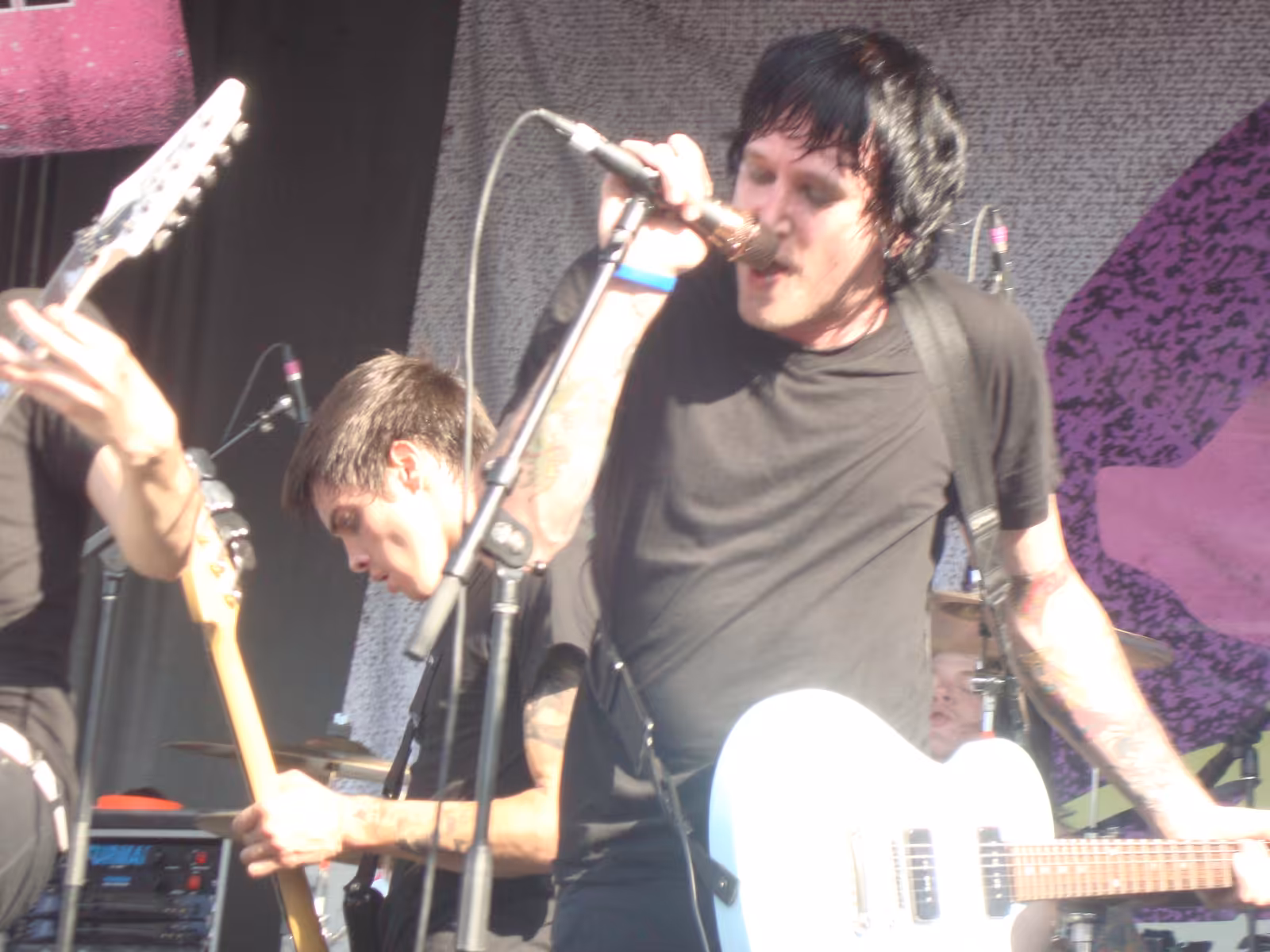 A band performing on an outdoor stage in front of a large crowd at the Vans Warped Tour in 2010.